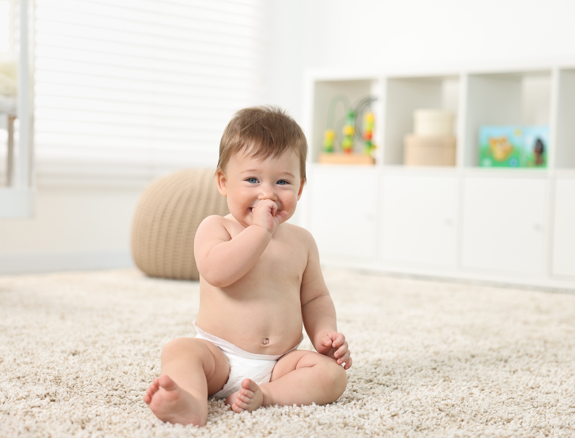 Smiling infant sitting in the middle of a room, looking at the camera