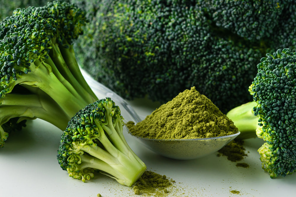 Image of broccolis with a heap tablespoon of broccoli powder on the side