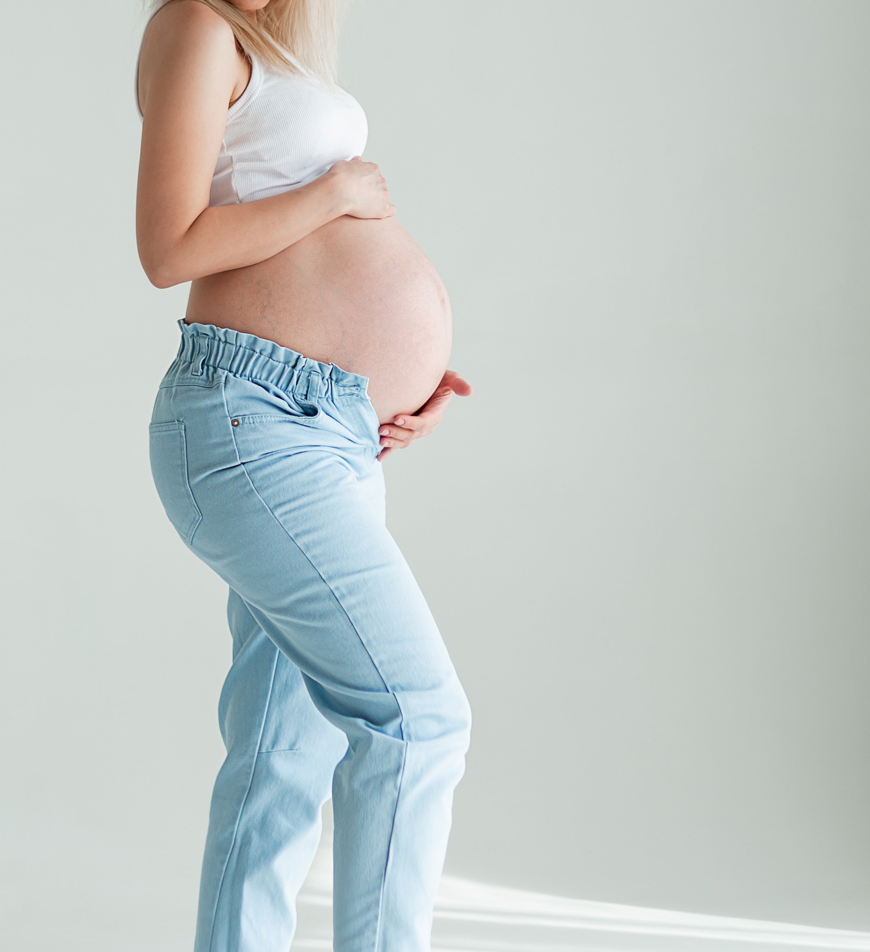 Pregnant woman gently holding and showing her belly, highlighting her baby bump