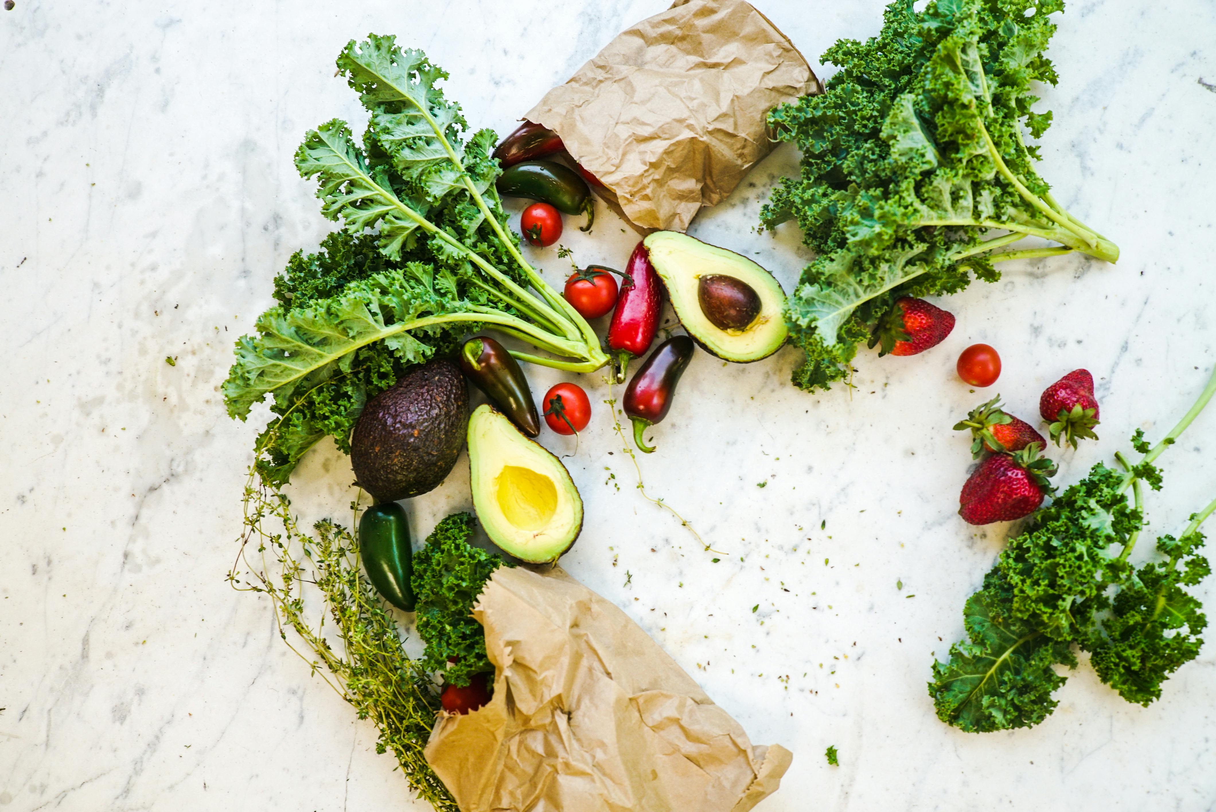 fruits like strawberry and tomato and vegetables like kale, avocado and green chilli with paper bags positioned into a wreath shape  
