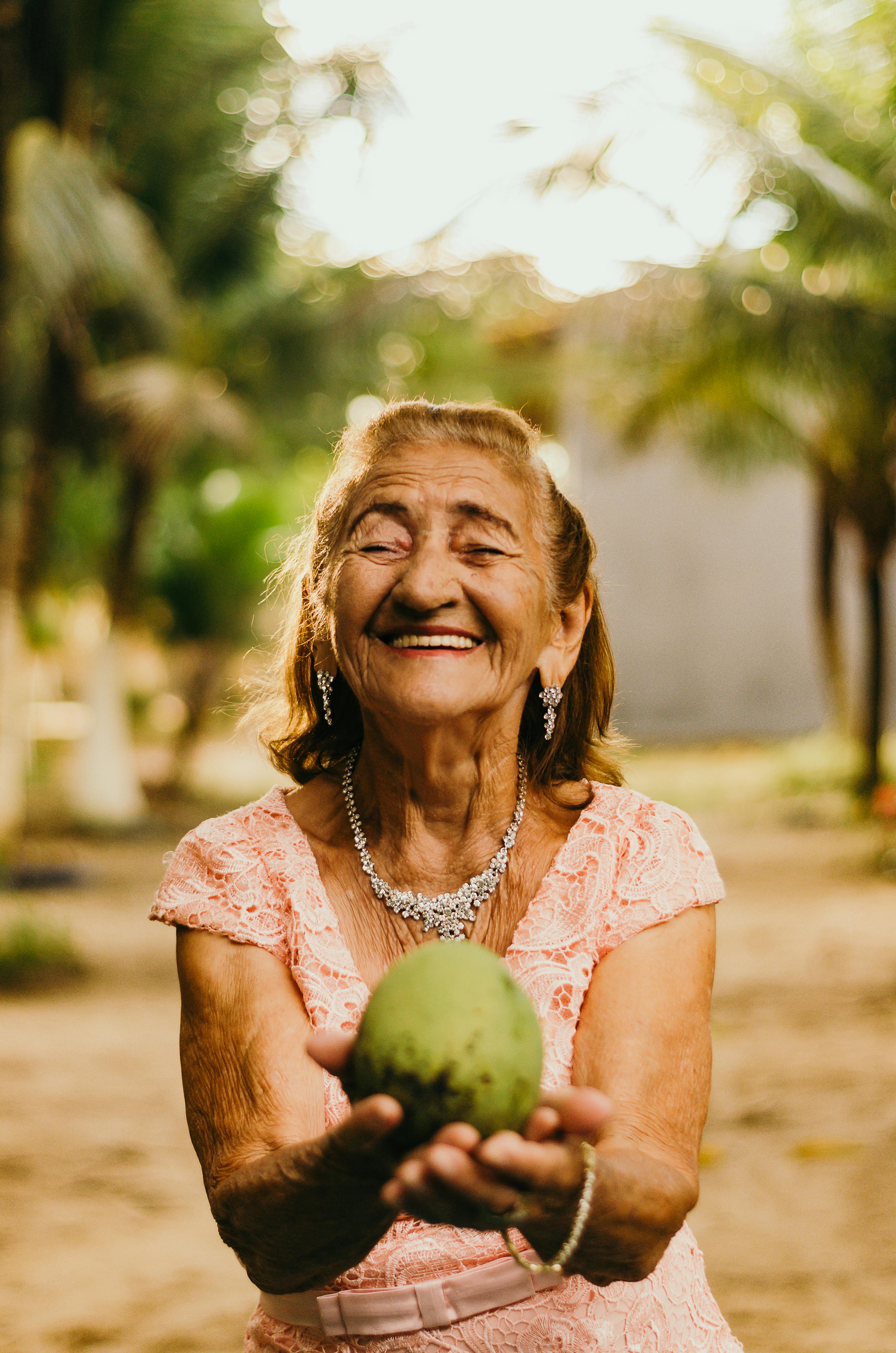 Woman holding a green fruit outdoors with trees in the background